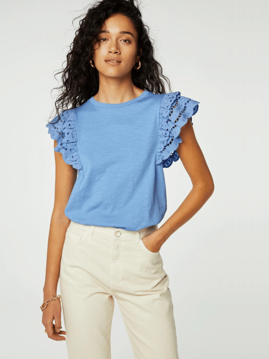 Die Frau trägt ein hellblaues T-Shirt von Fabienne Chapot mit Schmetterlingsärmeln aus Spitze und rundem Halsausschnitt zu einer hellbeigen Hose. Das T-Shirt besteht zu 100 % aus Bio-Baumwolle.